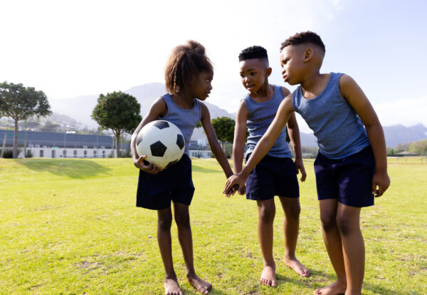 Happy african american schoolchildren playing football on field at school. Elementary school, sports, education and learning concept.