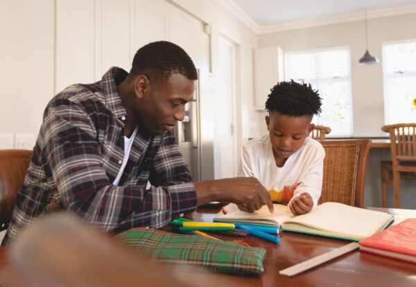 Front view of African American father helping his son with homework at table in a comfortable home